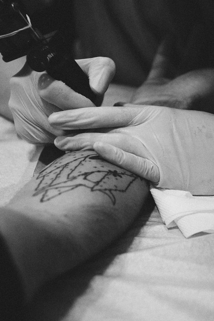 Close-up black and white photo of a tattoo artist working on an arm in a studio.
